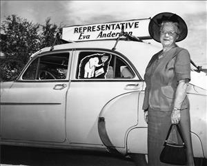 A woman in a hat and dress suit, holding a purse, stands next to a car with a sign on top that says Representative Eva Anderson. There's a drawing of an elephant holding flowers in the window of the car above a sign that says Eva. 